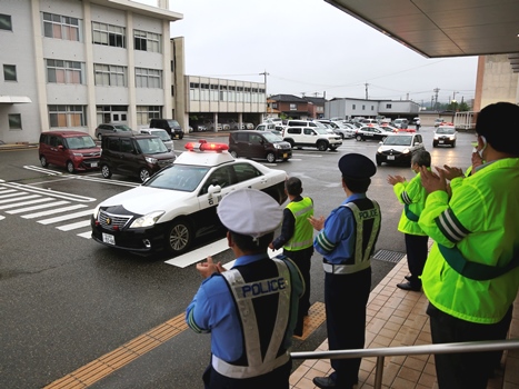 出動するパトカーを見送る関係者の画像