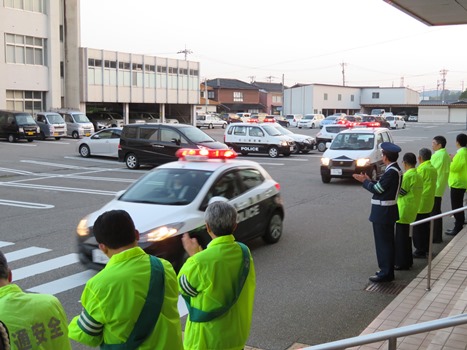 出動するパトカーを見送る関係者の画像